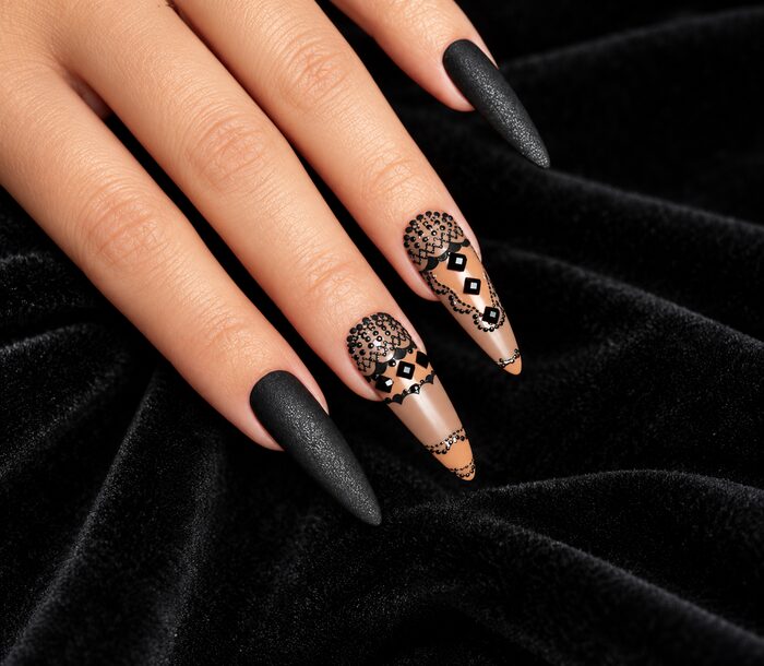 Matte black stiletto nails with hand-painted black lace on a nude accent nail