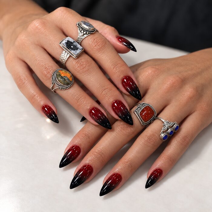 Red-to-black ombré on long stiletto nails, styled with statement rings